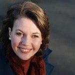 A working mum in a blue coat and scarf smiling, finding work-life balance.