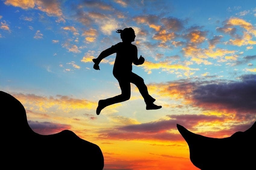 A silhouette of a woman *jumping* over a cliff at sunset. A silhouette of a woman *jumping* over a cliff at sunset.