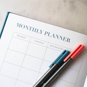 A monthly planner with pens on top used for organization.