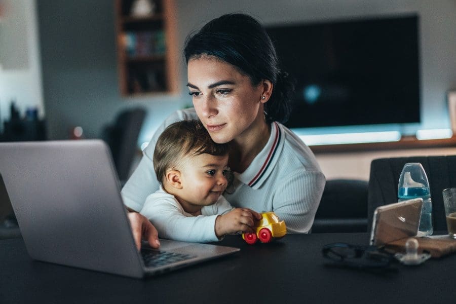 A woman is multitasking with a laptop and a baby, considering new careers after having a child. A woman is multitasking with a laptop and a baby, considering new careers after having a child.