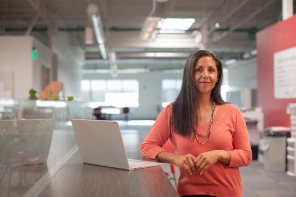 A woman returning to work after a birth injury stands in front of a desk with a laptop.