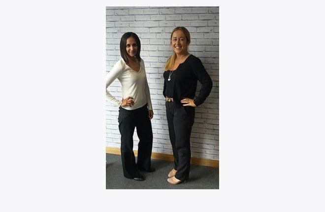 Two women returners standing next to each other in front of a wall, discussing their working jobs.