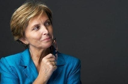 A woman, wearing a blue suit, is inspecting her chin.