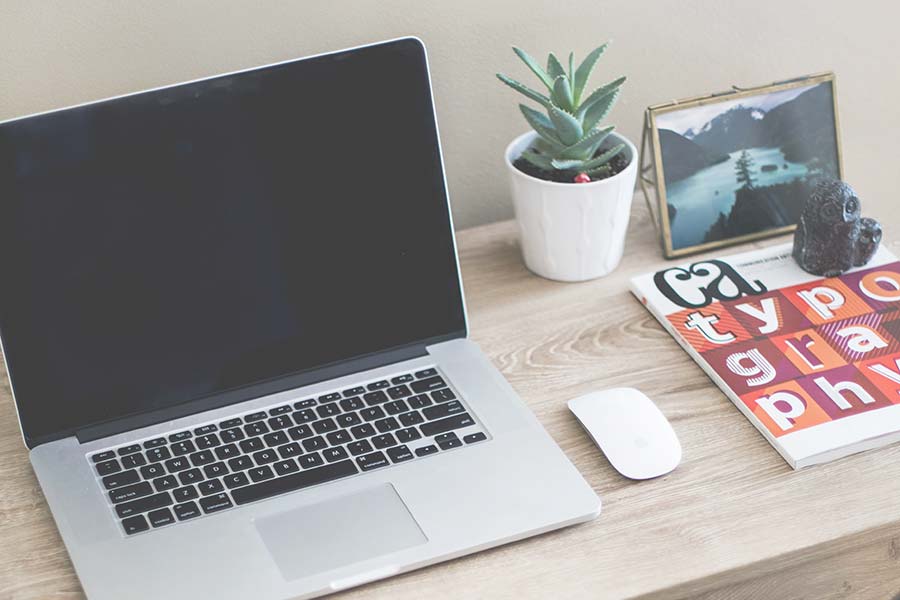 A laptop, wireless mouse, potted succulent, framed landscape photo, and a magazine are arranged on a light wood desk—creating an inspiring workspace for career growth or productive work sessions.