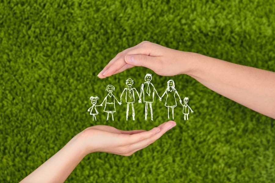 A mum’s hand holding a drawing of a family on green grass. A mum's hand holding a drawing of a family on green grass.