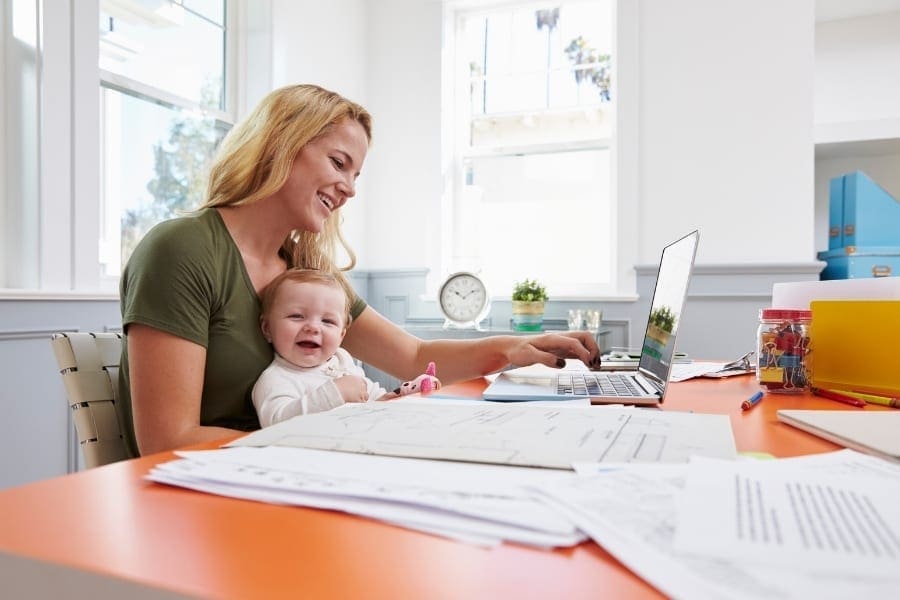 A working woman at her desk with a baby at her side.