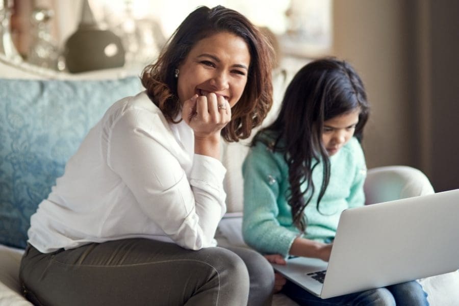 A working woman and her daughter sitting on a couch, finding work-life balance while using a laptop.