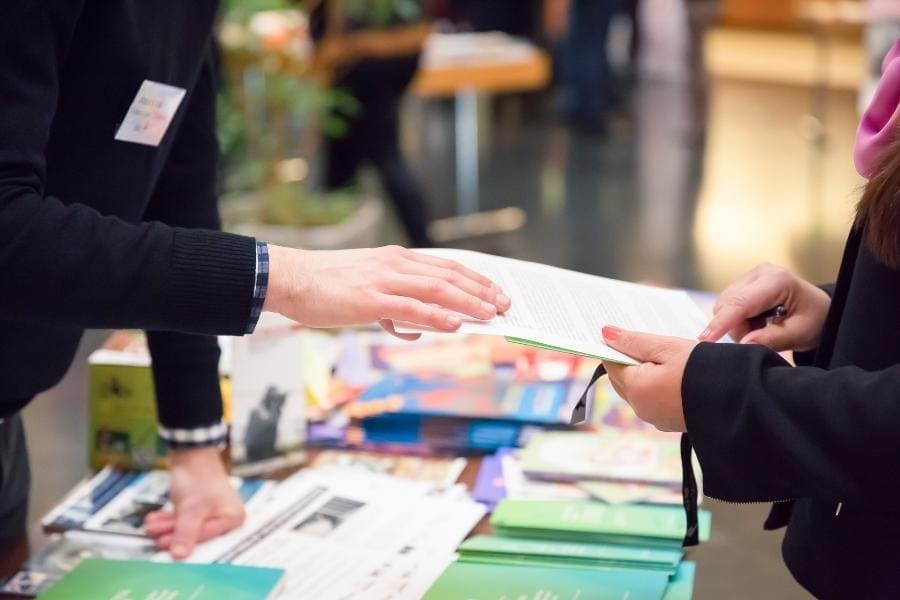 A working woman handing a book to a man at an event.