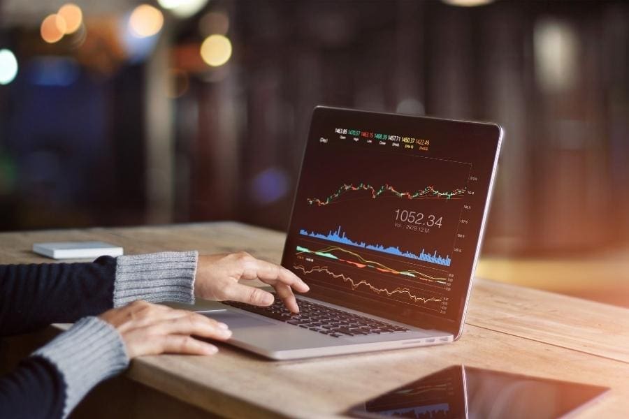 A person using a laptop to review stock chart while managing their work-life balance.