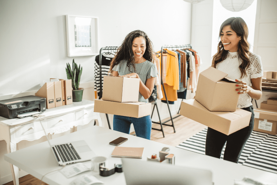 Two women returners standing in front of a desk with boxes, discussing work-life balance and job opportunities.
